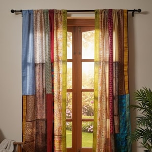 Op de afbeelding: Patchwork gordijnpanelen in tinten blauw, rood, groen en goud hangen voor een houten deur. De gordijnen zijn gemaakt van verschillende stoffen met patronen. Een houten stoel met een deken en een plant in een pot staan in de kamer.