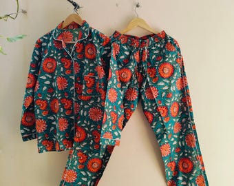 May include: A teal blue and orange floral print pyjama set with a collared top and long trousers. The set has white piping around the edges.