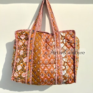 May include: A large, quilted tote bag with a patchwork design. The bag is made of brown fabric with floral patterns and red and white stripes. The bag has two long straps and is hanging on a white hook.