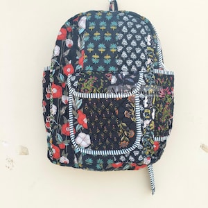 May include: A black quilted backpack with a floral print and a large front pocket. The backpack has a white and black striped trim.
