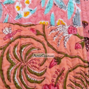 May include: Close-up of a quilted fabric with a floral pattern. The design features pink, peach, yellow, and green hues. The fabric is stitched with a repeating pattern. The text "Artist Couture" is visible.