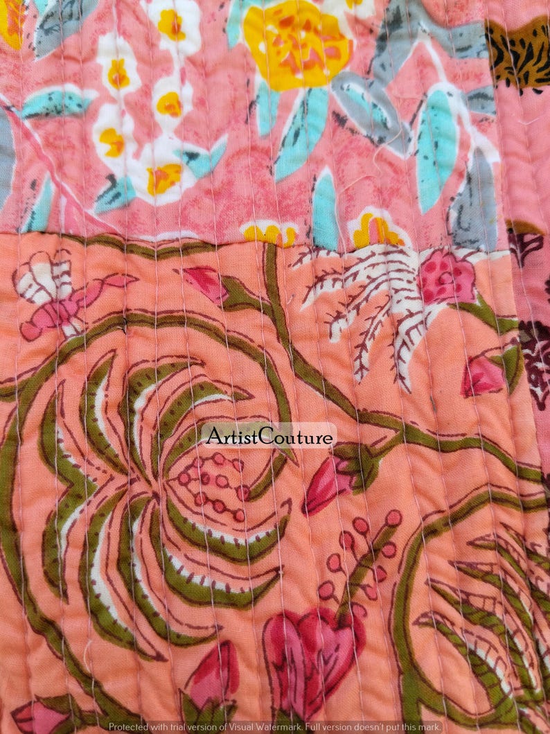 May include: Close-up of a quilted fabric with a floral pattern. The design features pink, peach, yellow, and green hues. The fabric is stitched with a repeating pattern. The text "Artist Couture" is visible.