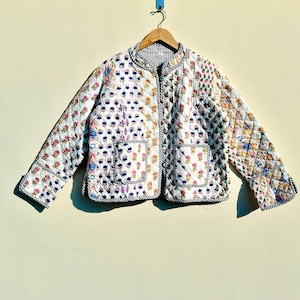 May include: A white quilted jacket with a floral print and black trim. The jacket has a zip closure and two pockets.
