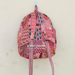 May include: Pink backpack with a patchwork design featuring floral and animal patterns. The backpack has adjustable straps and a top handle. The text "Artist Couture" is visible on the front.