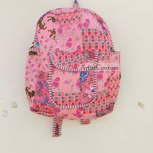 May include: A pink patchwork backpack with a floral and tiger print. The backpack has a large pocket on the front and adjustable straps. The text "Artist Couture" is printed on the front of the bag.