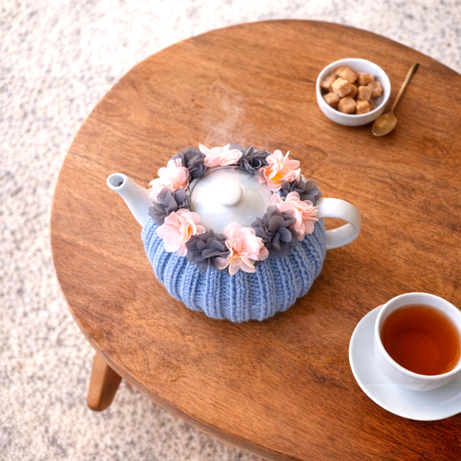 かぎ針編みのティーコージー、ピンクとグレーの花が描かれた青い