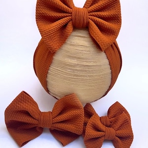 May include: Three brown fabric hair bows. The largest bow is on a headband, and the two smaller bows are separate.