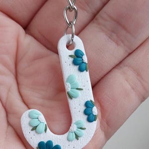 May include: White letter J keyring with a silver chain. The letter is decorated with blue and green flowers.