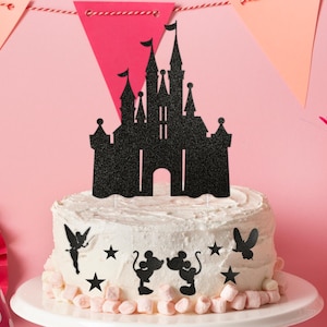 Puede incluir: Topper de pastel de castillo negro con purpurina sobre un pastel blanco decorado con un hada negra, estrellas y figuras de Mickey Mouse.