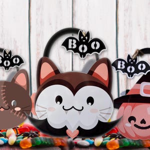 May include: Three Halloween-themed treat buckets. One is a brown cat with stitches, another is a vampire cat, and the last is a pumpkin wearing a witch hat. Each bucket has a black handle and a bat with the word "BOO" on it.
