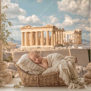 May include: A newborn baby sleeps peacefully in a woven basket, draped in a soft, cream-colored blanket. The background features a classical architectural scene with columns and a building, under a blue sky with clouds. A decorative olive tree is on the left.