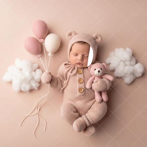 May include: A newborn baby in a light pink knitted bear suit and hat, holding a pink teddy bear and three balloons. The balloons are pink and white. The baby lies on a light pink background with white cloud decorations.