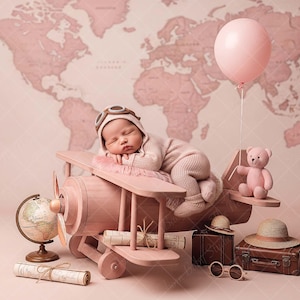 May include: A newborn baby wearing a pilot hat and outfit, sleeping on a pink wooden airplane prop. A pink teddy bear, globe, and vintage suitcase are nearby, with a pink balloon and a world map backdrop.