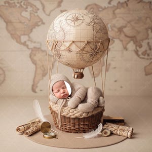 May include: A newborn baby in a knitted outfit and hat, nestled in a woven basket beneath a globe-shaped hot air balloon. The background features a vintage world map, with rolled scrolls, a compass, and feathers.