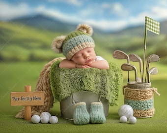 May include: A newborn baby wearing a green and blue knit hat with pom-poms, resting in a metal bucket lined with green fabric. Golf clubs, golf balls, and a sign that reads "Par-fectly New" are also in the image. The background is a blurred green field.