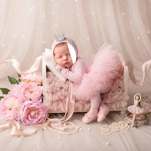 May include: A baby in a pink tutu and crown-adorned cap, asleep in a small bed. The image features pink flowers, ribbons, and pearls, creating a soft, dreamy aesthetic. The scene evokes a sense of delicate beauty.