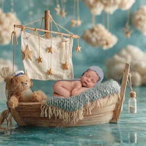 Puede incluir: Un recién nacido dormido yace en un barco de madera, sobre una manta de punto azul. Un osito de peluche con gorro de marinero está sentado al lado. El barco tiene una vela con decoraciones de estrellas, sobre un fondo de nubes y un faro.