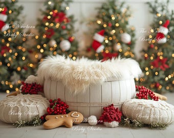 May include: A festive newborn photography prop arrangement. A white wooden basket with a fluffy lining is surrounded by decorations, including knitted cushions, red berries, a gingerbread biscuit, and miniature Santa hats. Lit Christmas trees are in the background.
