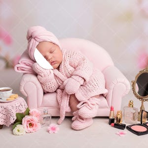 May include: A newborn baby dressed in a pink knitted robe, hat, mittens, and booties, resting on a miniature pink sofa. A small table with a teacup, cookies, and flowers is nearby, along with a vanity mirror and makeup items.