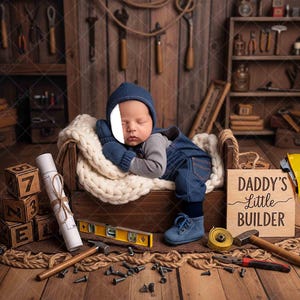Peut inclure: Un bébé en salopette en jean et bonnet bleu dort dans un lit en bois. Une pancarte indique "Daddy's Little Builder". Des outils de construction et des blocs de bois entourent le lit, créant un thème de construction.