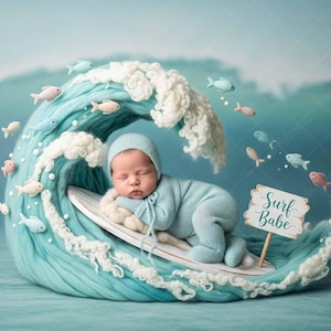 May include: A newborn baby in a light blue knit outfit and matching cap, sleeping peacefully on a surfboard. The baby is nestled in a turquoise wave with white foam, surrounded by small fish and a sign that says "Surf Babe."