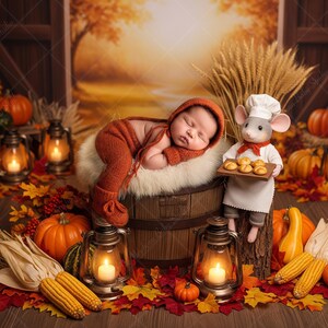 May include: A newborn baby in an orange knit outfit sleeps on a fluffy white surface atop a wooden barrel, surrounded by autumn decor. A mouse chef holds a tray of baked goods. Pumpkins, corn, and lanterns complete the fall scene.
