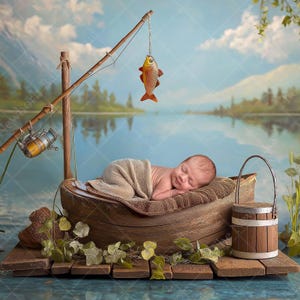 May include: A newborn baby sleeps peacefully in a wooden boat, part of a photography prop set. A fishing rod with a toy fish hangs above. The scene is set against a backdrop of a lake and mountains, with a wooden bucket nearby.