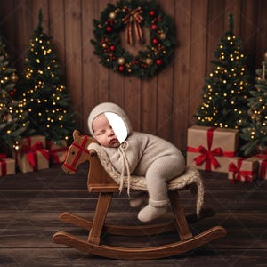 Puede incluir: Un bebé dormido, vestido con un conjunto y gorro beige, descansa sobre un caballito de madera. El fondo presenta árboles de Navidad con luces brillantes, regalos envueltos y una corona festiva, creando una escena navideña acogedora.