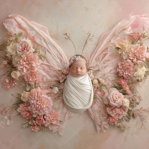 May include: A newborn baby wrapped in white fabric, posed as the body of a butterfly. The wings are created with pink fabric and adorned with pink and cream-colored flowers and greenery. The background is a soft, textured pink.