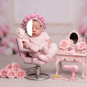 May include: A newborn baby wearing a pink outfit and hair rollers sits in a pink salon chair. A miniature pink vanity with a mirror, roses, and a hairdryer is nearby. A bouquet of pink roses is in the foreground.