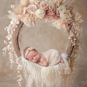 Pode incluir: Um recém-nascido dorme tranquilamente em um baloiço floral. O baloiço é adornado com uma grinalda de flores em tons de rosa, creme e bege. O bebé está envolto numa manta macia cor creme e usa uma faixa de cabeça a condizer.