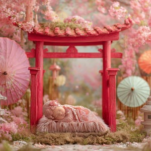 May include: A newborn baby lies peacefully in a Japanese-themed setting. The scene features a red torii gate, pink parasols, and stone lanterns, all surrounded by cherry blossoms. The baby is wrapped in a pink blanket.