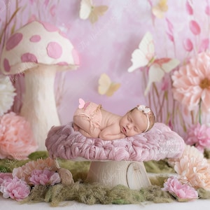 May include: A newborn baby lies peacefully on a plush, pink mushroom prop, surrounded by floral decorations and butterflies. The backdrop features a soft pink and white color scheme, creating a whimsical and dreamy scene for newborn photography.