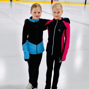 Könnte beinhalten: Zwei junge Mädchen tragen schwarze Jacken mit bunten Akzenten. Das Mädchen links trägt eine blaue und schwarze Jacke mit einem hellblauen Akzent. Das Mädchen rechts trägt eine schwarze und pinkfarbene Jacke mit einem weißen Buchstaben K auf der Brust. Beide Mädchen tragen schwarze Hosen.