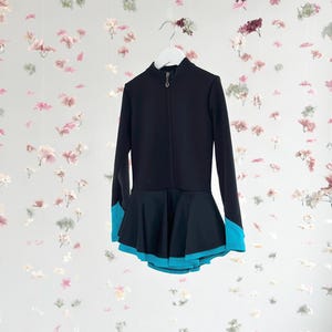 Könnte beinhalten: Schwarzes Eiskunstlaufkleid mit langen Ärmeln und einem blauen Saum am unteren Rand des Rocks.