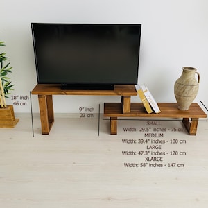 K&ouml;nnte beinhalten: Ein TV-St&auml;nder aus Holz mit zwei Regalen. Der St&auml;nder ist 23 cm breit und 46 cm hoch. Das obere Regal ist 75 cm breit, das untere Regal ist 100 cm breit. Der St&auml;nder ist aus Naturholz gefertigt und hat einen rustikalen Look. Der St&auml;nder ist perfekt f&uuml;r einen kleinen Fernseher oder andere Elektronik.