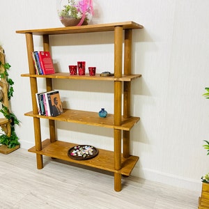 May include: A wooden bookshelf with four shelves and four posts. The shelves are filled with books, decorative items, and a small plant. The bookshelf is made of natural wood and has a rustic look.