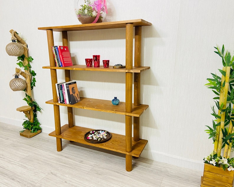 May include: A wooden bookshelf with four shelves and four posts. The shelves are filled with books, decorative items, and a small plant. The bookshelf is made of natural wood and has a rustic look.