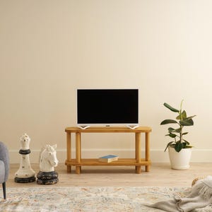 May include: A living room scene featuring a wooden TV stand with a black screen television. A gray armchair, decorative chess pieces, and a potted plant are also present. A rug and a woven ottoman with a blanket complete the decor.