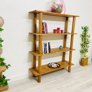 May include: A four-tier wooden shelf unit with a natural brown finish. The shelf is filled with books, decorative items, and a small potted plant.