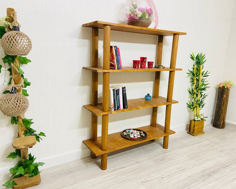 May include: A four-tier wooden shelf unit with a natural brown finish. The shelf is filled with books, decorative items, and a small potted plant.