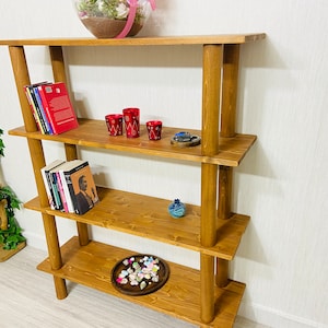 May include: A four-tier wooden shelf unit with rounded posts. The shelves are stained a dark brown color and are filled with books, decorative items, and a small tray of seashells.