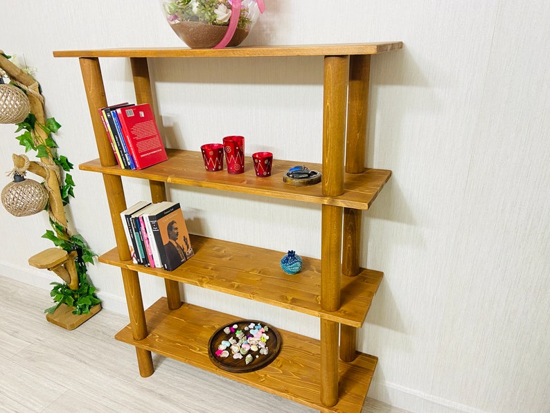 May include: A four-tier wooden shelf unit with rounded posts. The shelves are stained a dark brown color and are filled with books, decorative items, and a small tray of seashells.