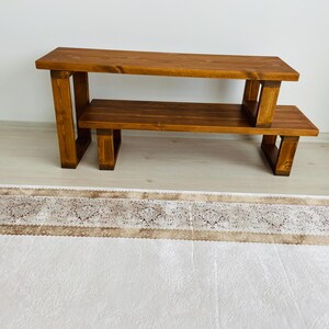 K&ouml;nnte beinhalten: Ein zweistufiges Holzregal mit naturbrauner Oberfl&auml;che. Das Regal hat eine rechteckige obere und untere Ablage mit offenen Seiten und einem rechteckigen Rahmen.