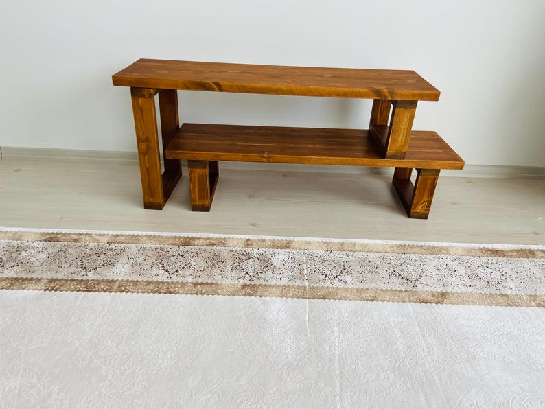 K&ouml;nnte beinhalten: Ein zweistufiges Holzregal mit naturbrauner Oberfl&auml;che. Das Regal hat eine rechteckige obere und untere Ablage mit offenen Seiten und einem rechteckigen Rahmen.