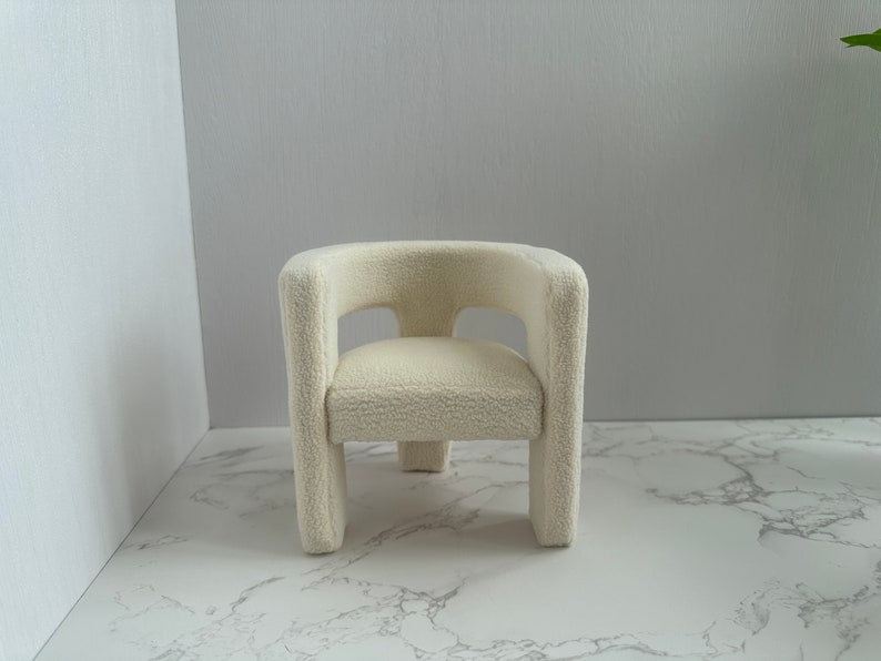 May include: A white plush armchair with a rounded back and a simple design. The chair is sitting on a white marble surface.