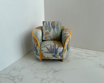 May include: A small armchair with a floral patterned fabric and yellow trim. The armchair has a cushion with a similar floral pattern.