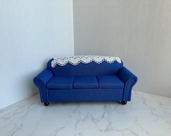 May include: A blue velvet sofa with a white crocheted throw on top. The sofa has a classic design with rolled arms and a tufted back.