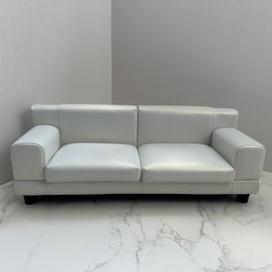 May include: A white leather sofa with a simple design. The sofa has two cushions and is sitting on a white marble floor.