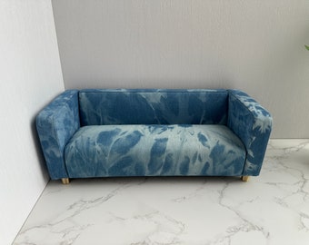 May include: A blue denim couch with a tie-dye pattern. The couch has a light blue background with darker blue swirls and a white outline. The couch has wooden legs.
